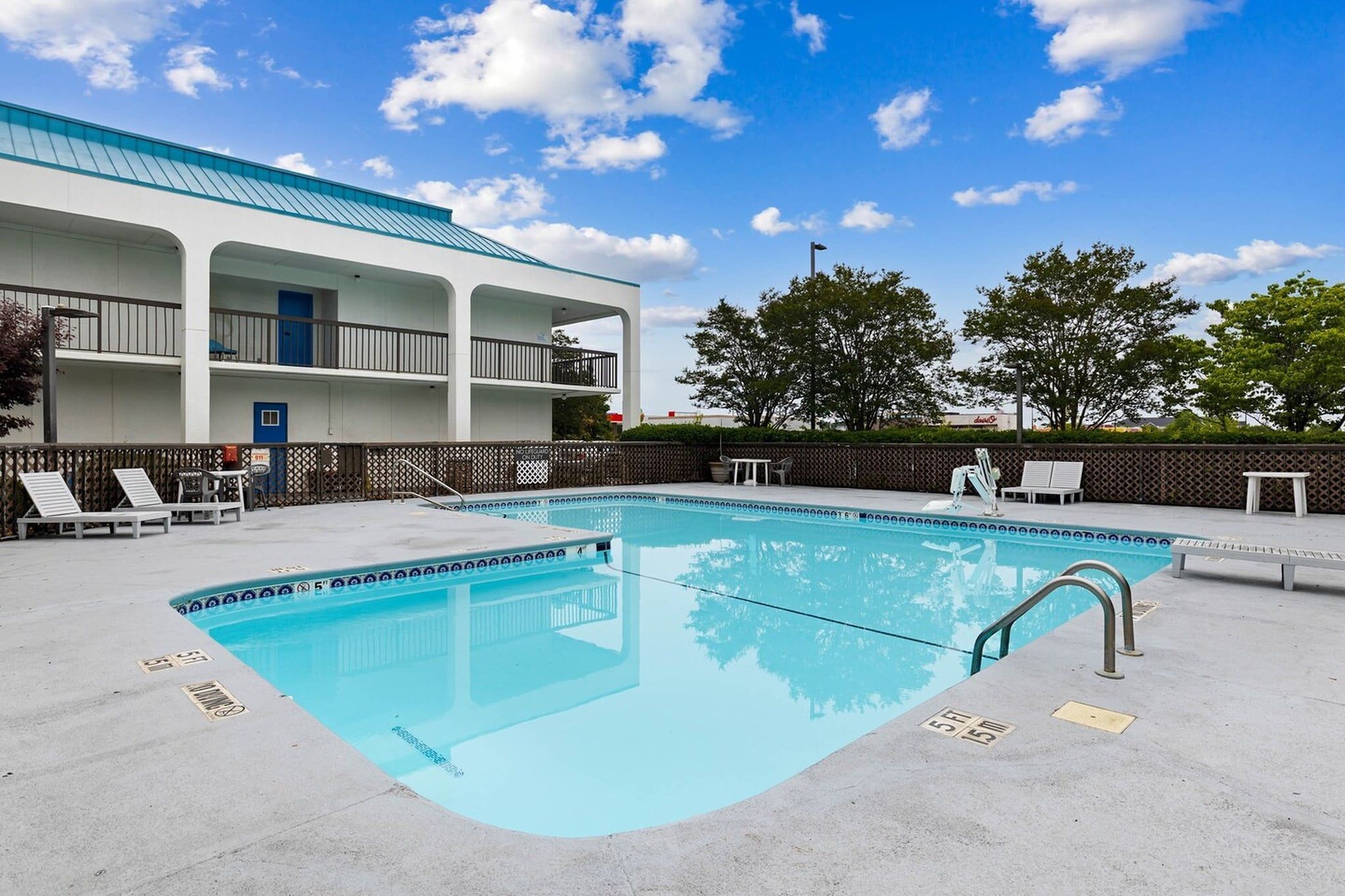 Une piscine à l’eau d’un bleu limpide, entourée d’une terrasse en béton. On y trouve des chaises longues et une petite table.