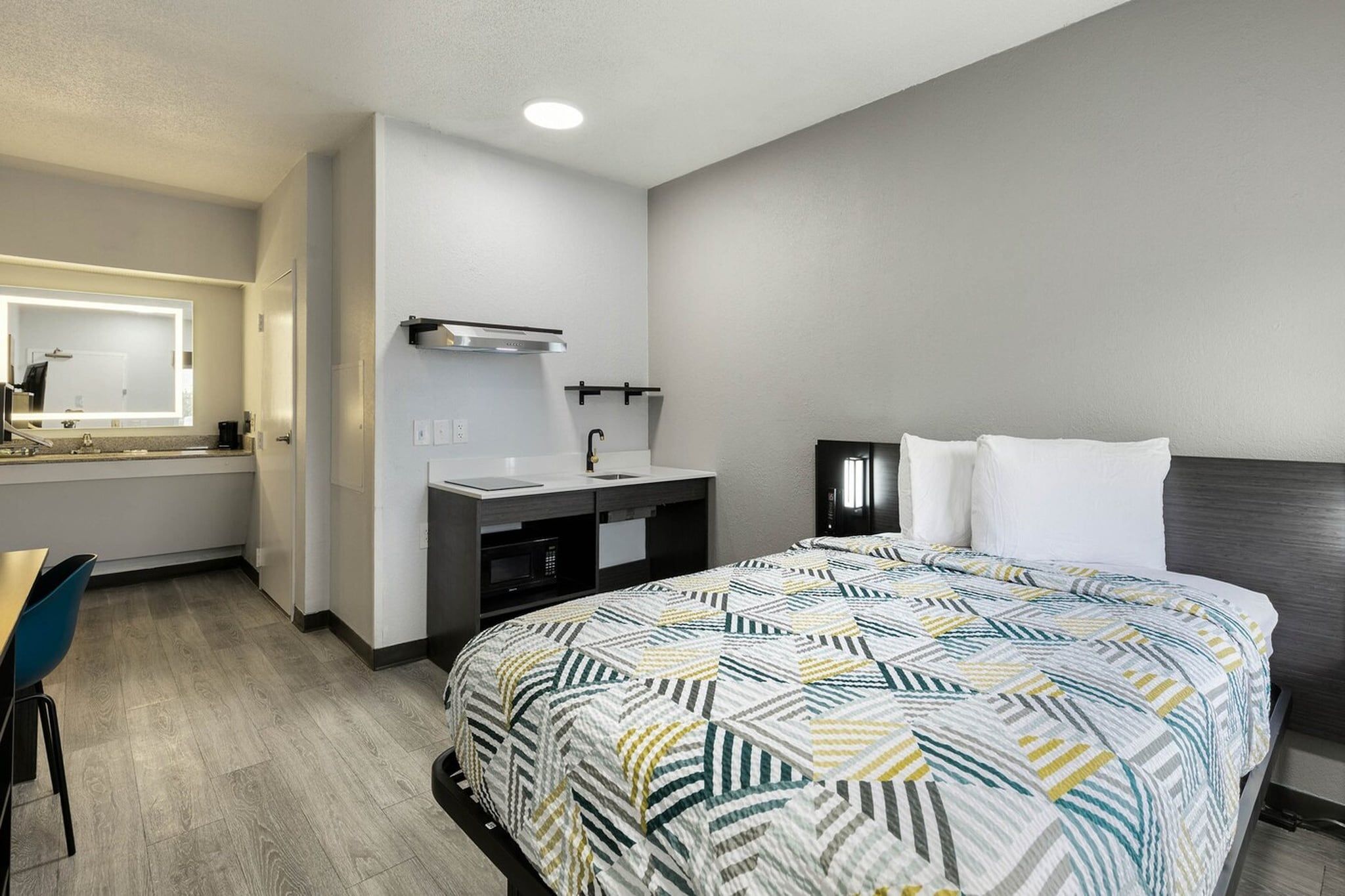 Quarto de hotel com cama, escrivaninha, toucador com espelho e mesa de cabeceira.