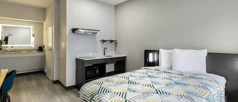 A hotel room with a bed, a desk, a vanity with a mirror, and a nightstand.