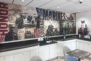 Ein Restaurantinneres mit einer großen Wandmalerei, die Militärszenen zeigt, sowie den Schriftzug 'MARINES' und das Wort 'Mut'.