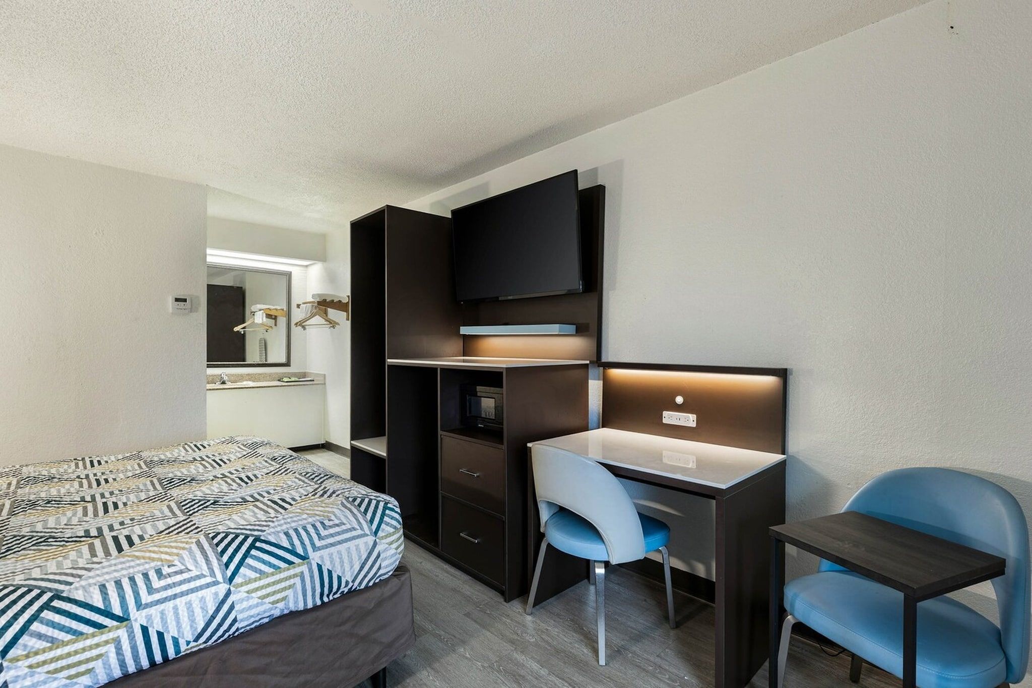 Ein Hotelzimmer mit einem Bett, einem Schreibtisch, einem Sessel, einem Fernseher und einem Spiegel.