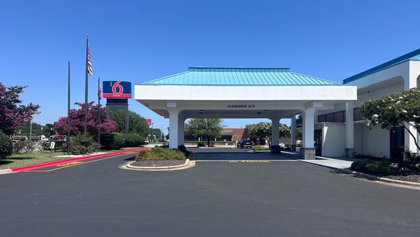 L’entrée d’un hôtel avec un espace de stationnement couvert, une enseigne indiquant la présence de six suites, et un ciel dégagé.