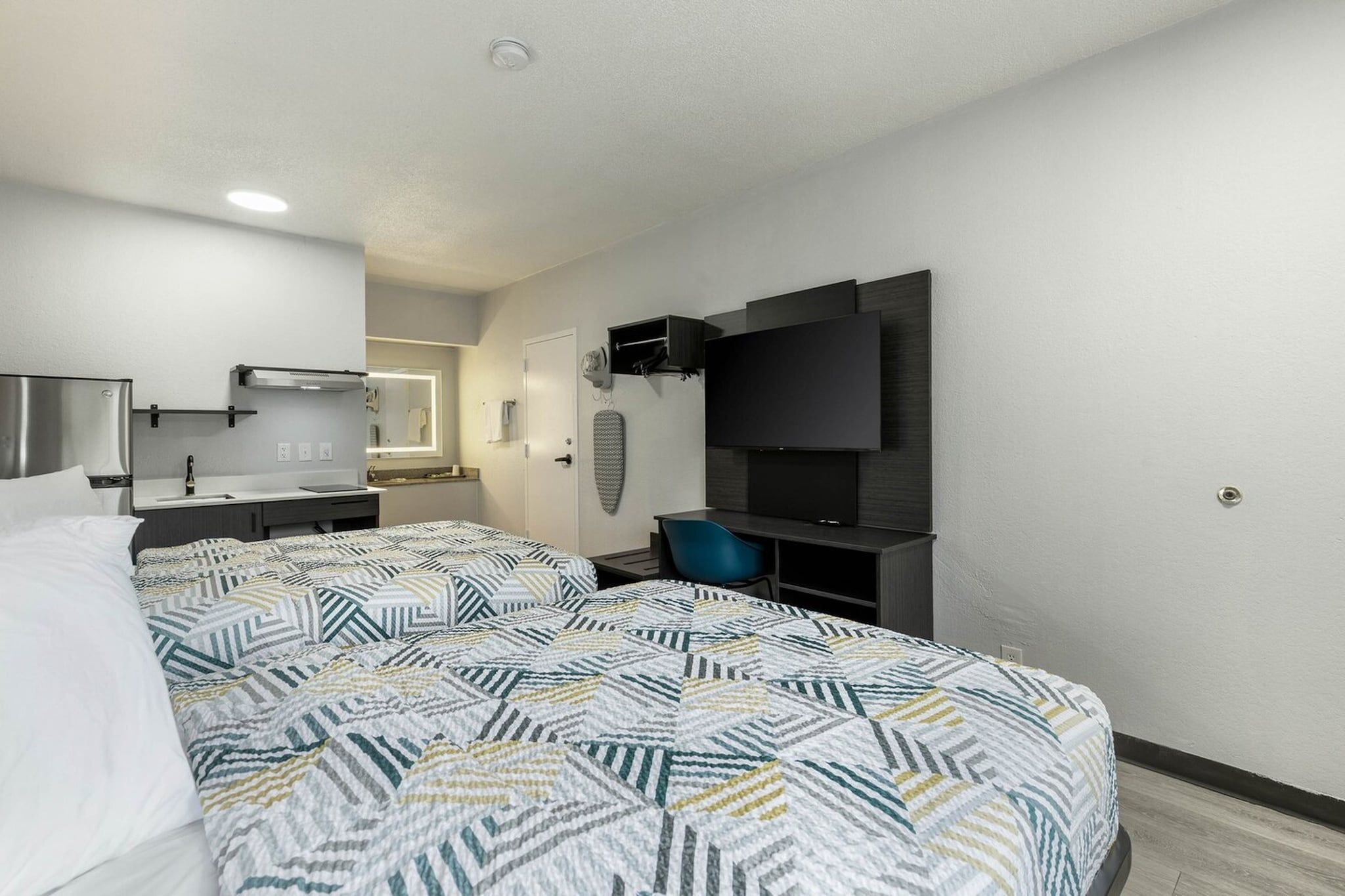 Hotellihuone, jossa on sänky, seinälle asennettu taulutelevisio, pieni työpöytä ja tuoli.