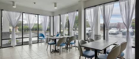 A conference room with a large table and chairs, large windows with curtains, and a view of a parking area.