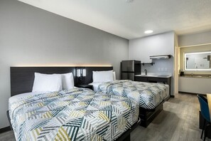 Una habitación de hotel con una cama doble, una kitchenette pequeña, un espejo y un escritorio.