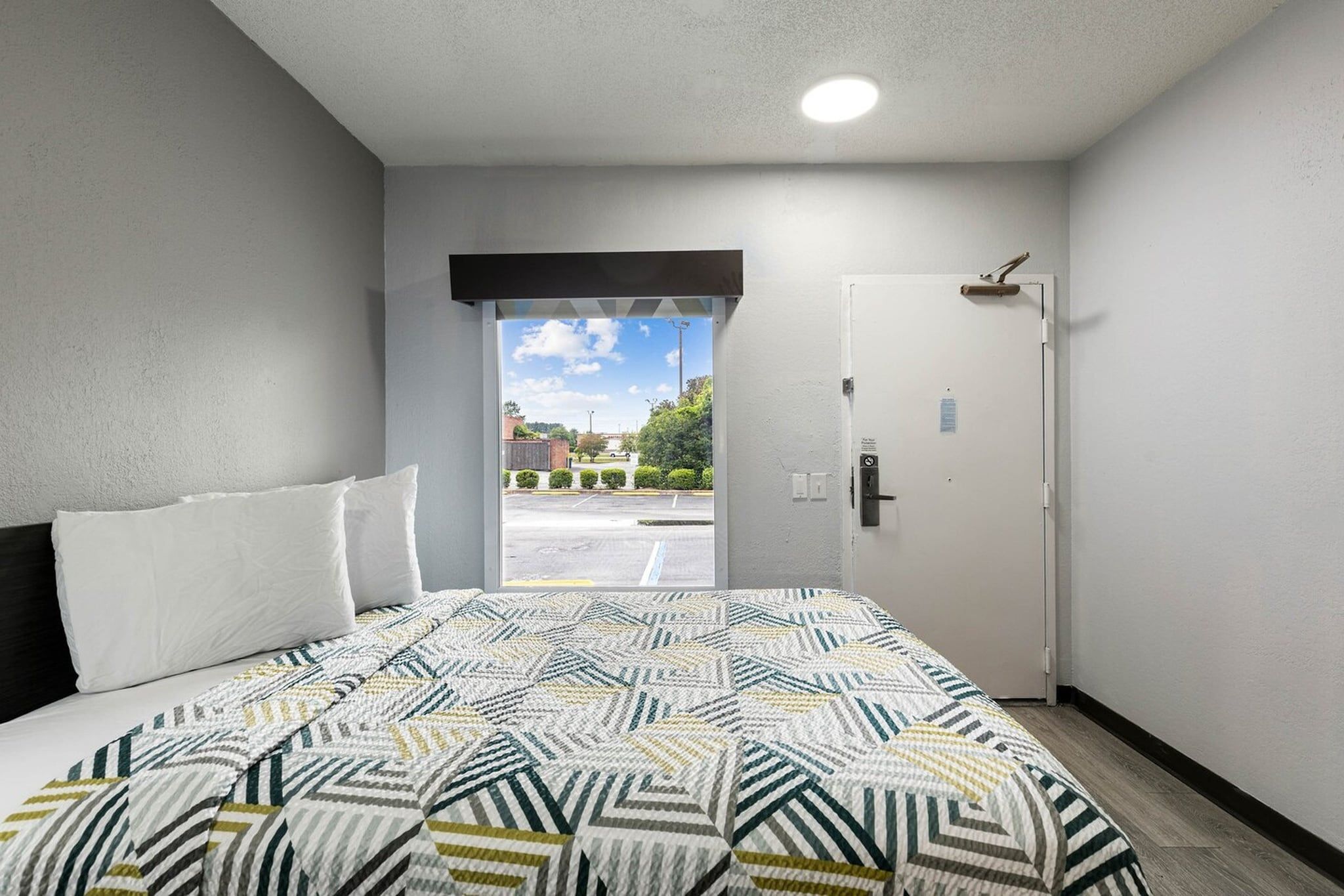 Quarto de hotel com cama, porta e vista para um estacionamento.