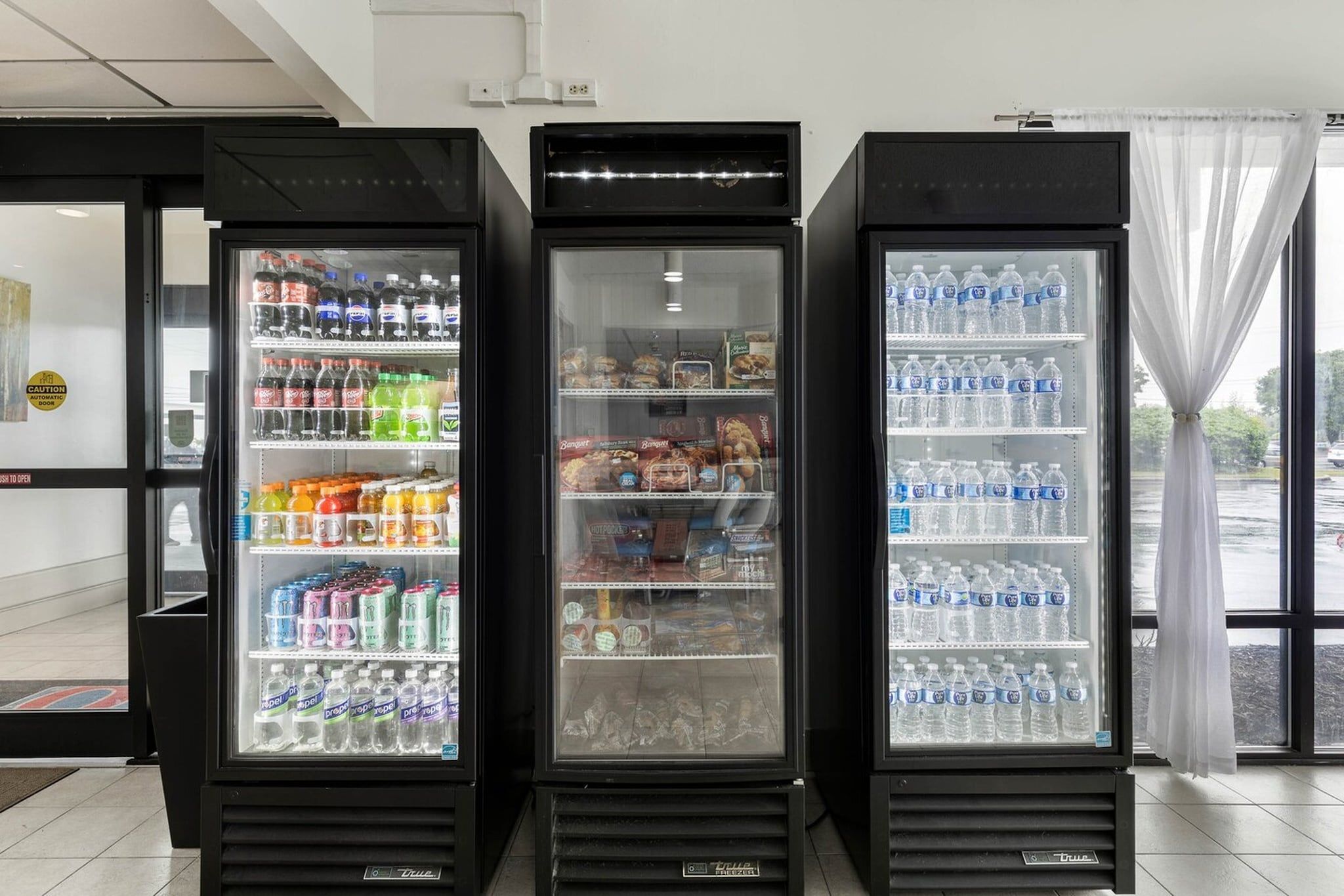 Three beverage vending machines with various drinks and snacks inside.