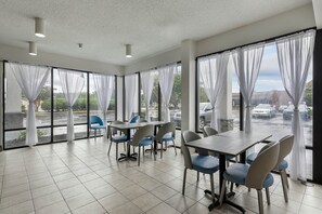 Une salle de conférence dotée d’une grande table et de chaises, de grandes fenêtres avec des rideaux et donnant sur un parking.