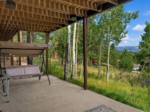 Eine Terrasse im Freien mit überdachter Sitzgruppe, einem Betonboden und Blick auf Bäume und Berge im Hintergrund.