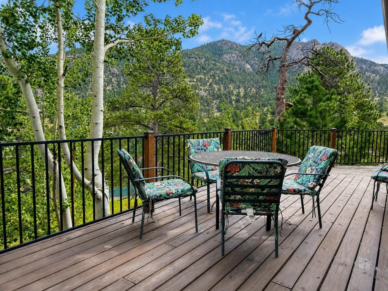 A deck with a table and chairs, surrounded by a metal railing, overlooking a mountainous landscape.