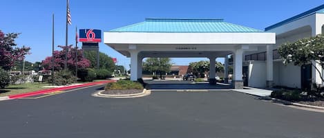Entrada de hotel con zona de estacionamiento techada, cielo despejado y un letrero que indica 6 suites.