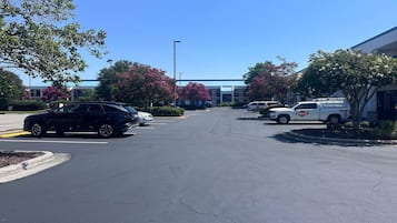 Ein Parkplatz mit mehreren Autos, ein Gebäude mit blauem Dach und Bäume mit rosa Blüten.