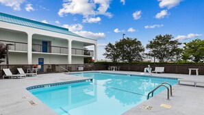 Une piscine avec des chaises longues et, au fond, un bâtiment surmonté d’un toit bleu.
