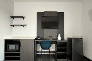 A modern office space with a desk, chair, shelves, a microwave, and a flat-screen TV.