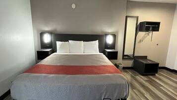 A hotel room with a bed, bedside tables, a mirror, and a wall-mounted TV.