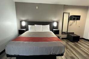 A hotel room with a bed, bedside tables, a mirror, and a wall-mounted TV. - 1 King Bed | Non-Smoking, Micfridge (Urbana, IL)