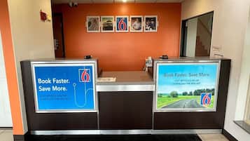 En receptionsdisk med to store skilte, der reklamerer for Motel 6 appen til booking og besparelser.