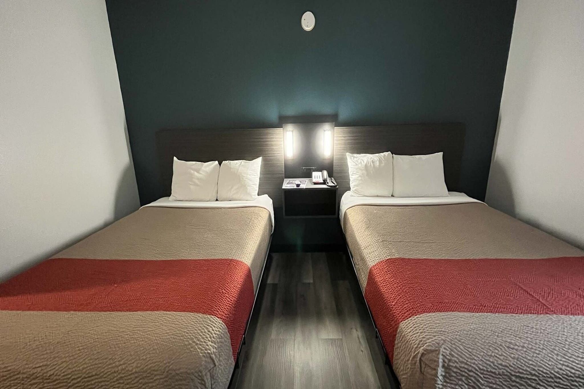 Habitación de hotel con dos camas, una mesita de noche con teléfono y lámpara, y una lámpara de pared.