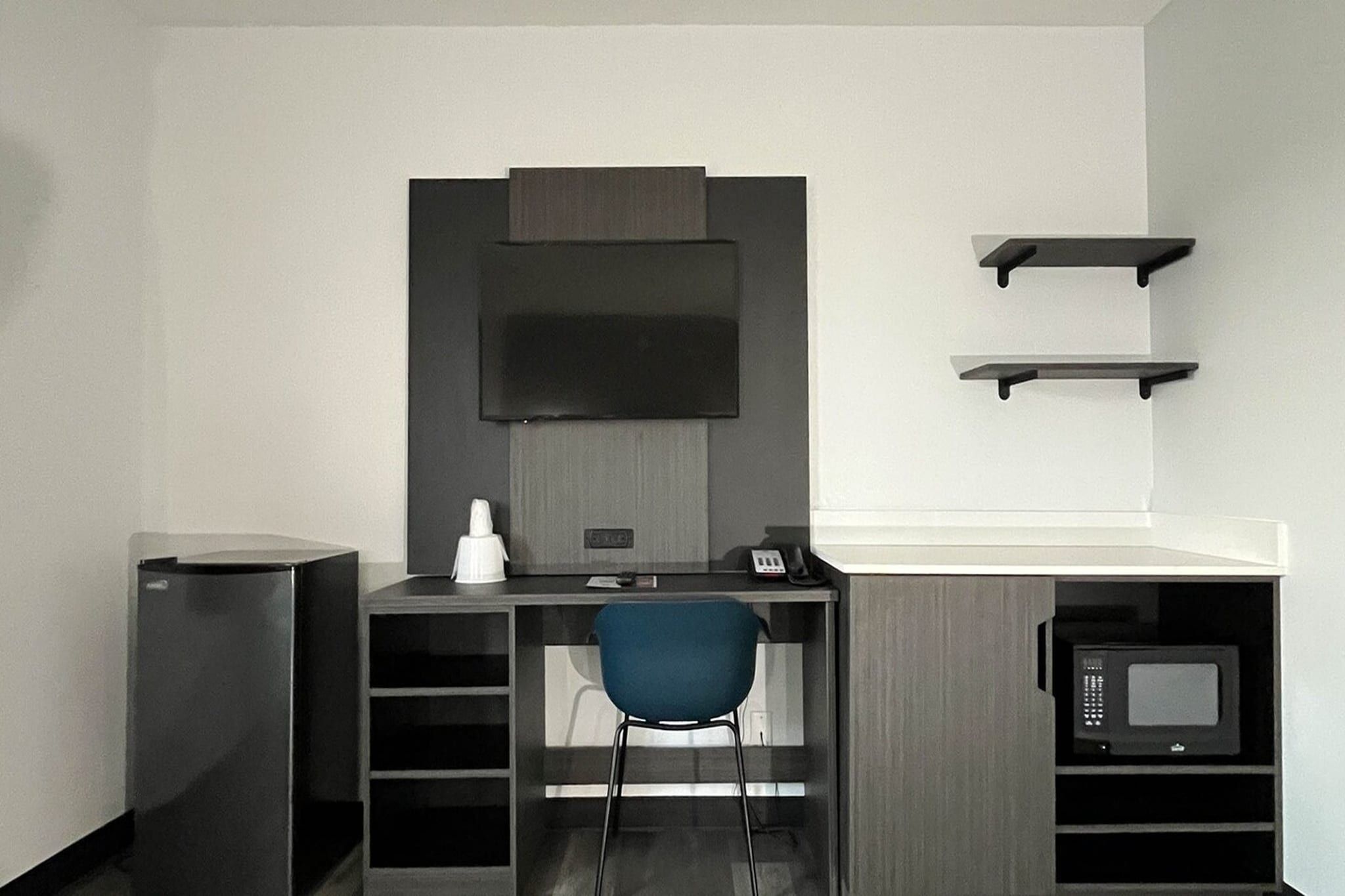 Un espacio de oficina pequeño con escritorio, silla, televisor montado y microondas.