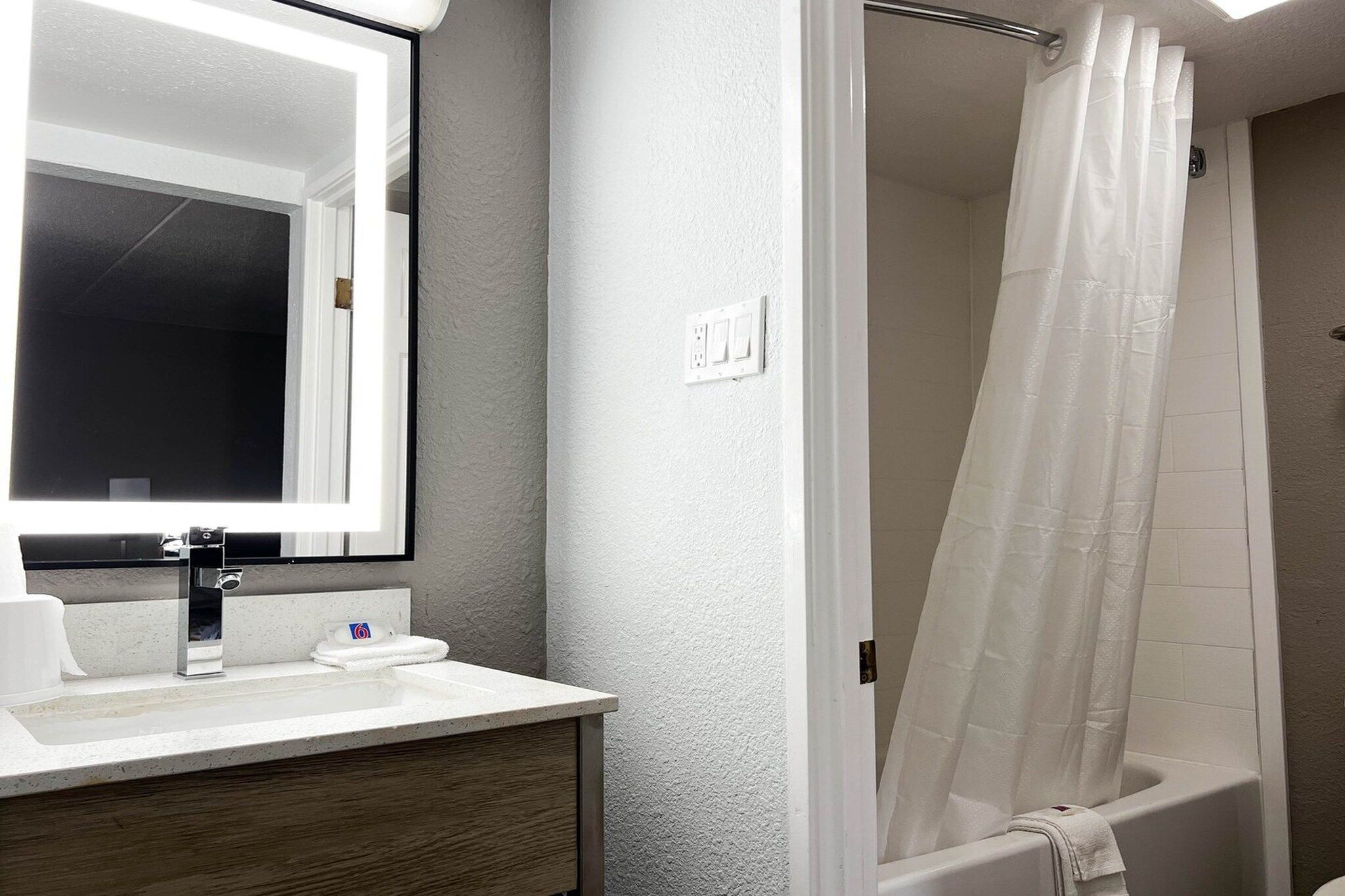 Une salle de bain avec un lavabo blanc, un miroir et une douche avec un rideau blanc.