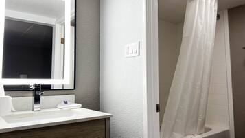 Une salle de bain avec un lavabo blanc, un miroir et une douche avec un rideau blanc.