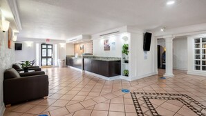 Un vestíbulo de hotel con mostrador de recepción, zona de estar y piso de baldosas.