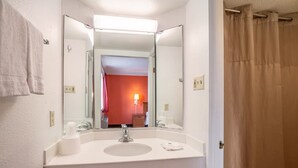 Un baño de hotel con un lavamanos blanco, un espejo, una toalla y una cortina de ducha.