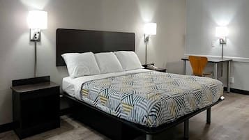 Quarto de hotel com cama, mesas de cabeceira, escrivaninha e duas luminárias fixadas na parede.