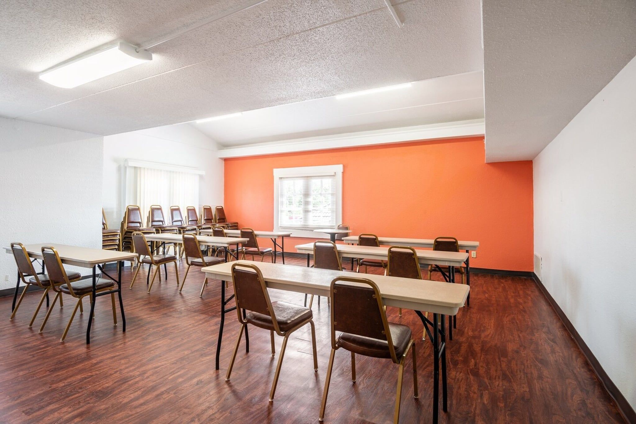 Une salle de conférence équipée de tables et de chaises, dotée d’une grande fenêtre et d’un mur d’accent de couleur orange.