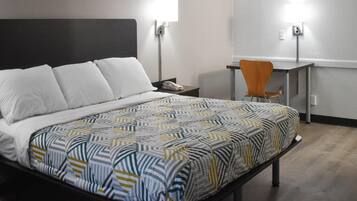 Une chambre d’hôtel comprenant un lit, une table de chevet, une chaise, un bureau et deux lampes fixées au mur.