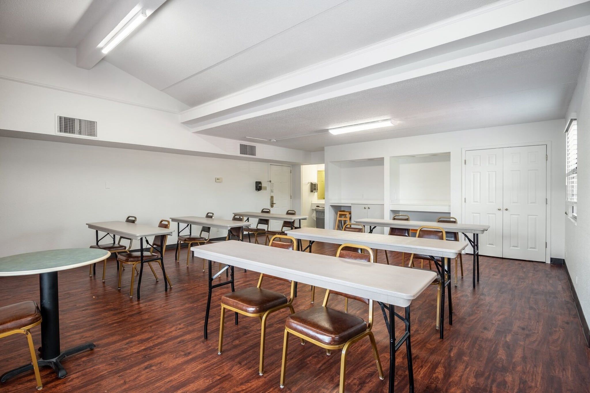 Une salle de conférence dotée de plusieurs tables et chaises, de murs blancs et d’un plancher en bois.
