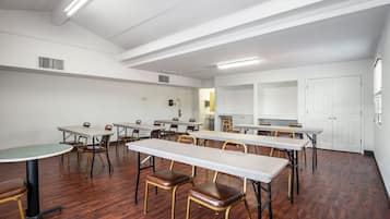 Une salle de conférence dotée de plusieurs tables et chaises, de murs blancs et d’un plancher en bois.