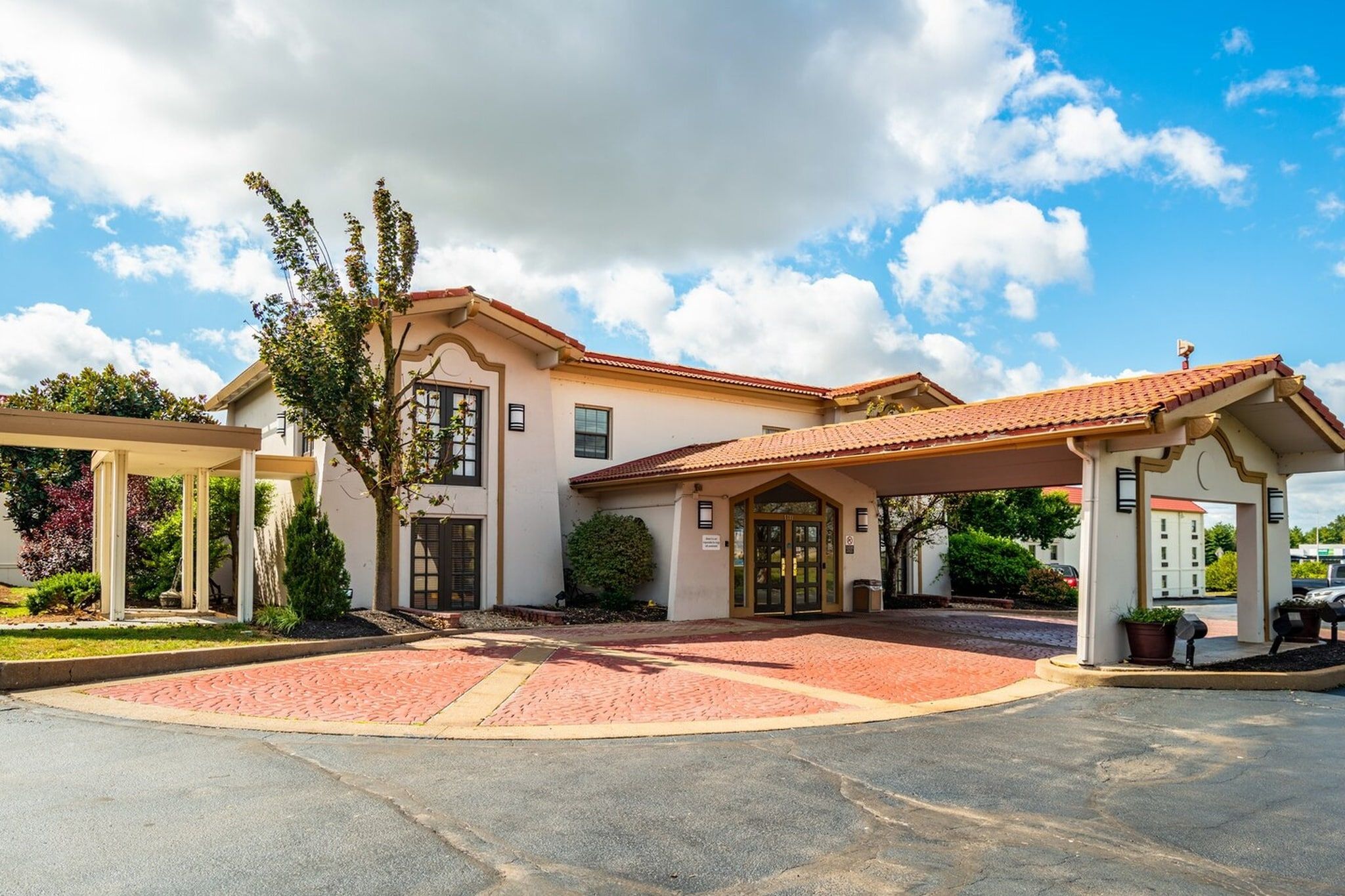 A two-story building with a red-tiled roof, a covered entrance, and a landscaped driveway.