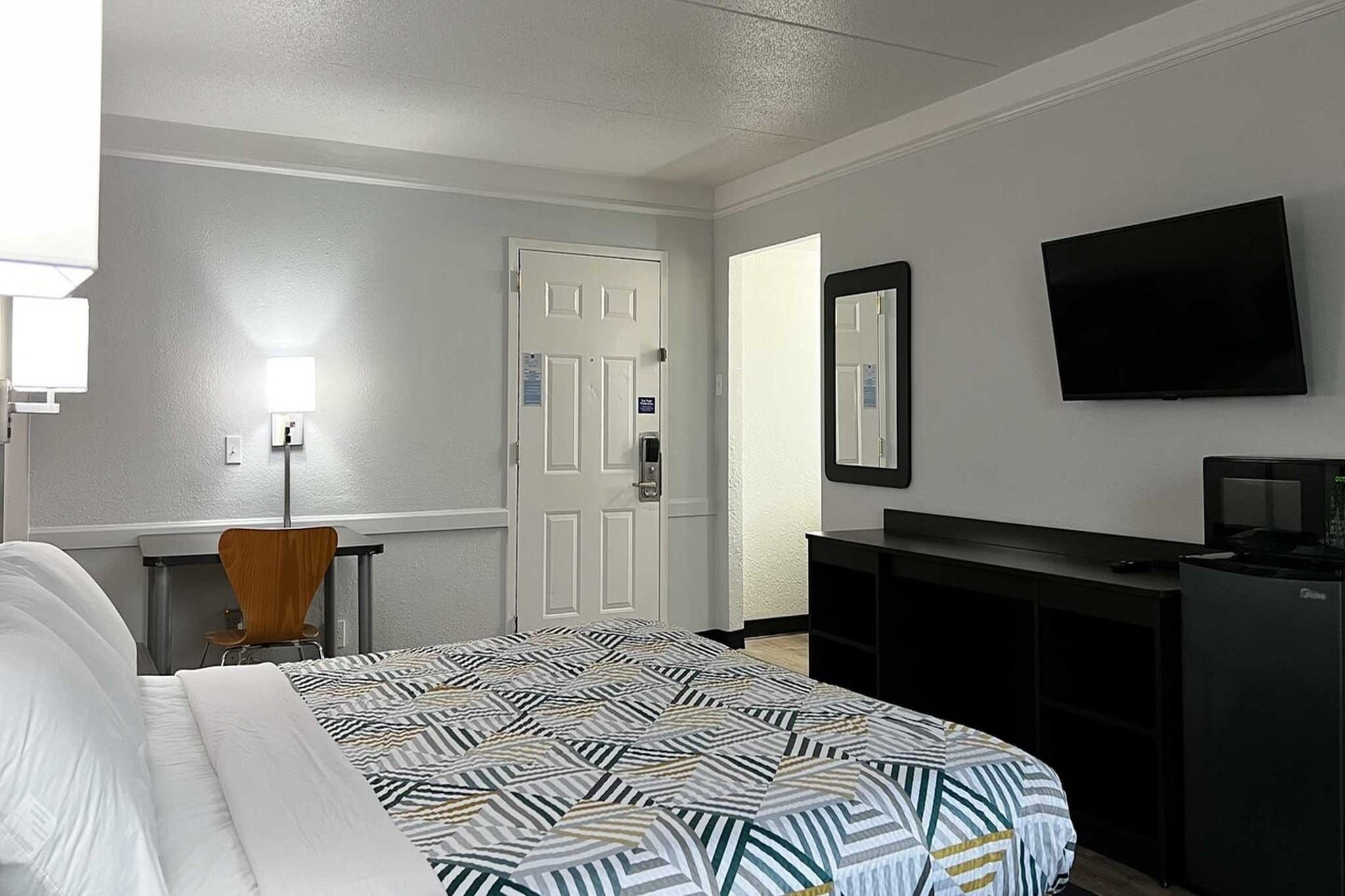 Une chambre d’hôtel avec un lit, un bureau, une chaise, une télévision et une porte.