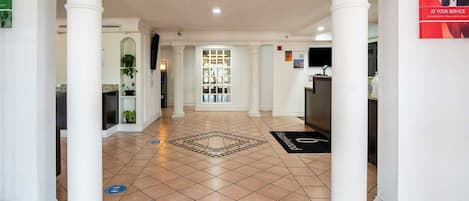 A hotel lobby with white columns, a reception desk, and a tiled floor.