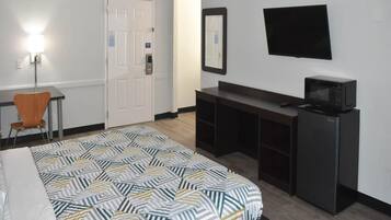 Une chambre d’hôtel équipée d’un lit, d’un bureau, d’une chaise, d’une télévision et d’un four à micro-ondes.
