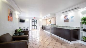 Un vestíbulo de hotel con una recepción, zona de estar y televisor montado en la pared.