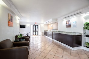 Eine Hotelhalle mit Rezeption, Sitzgelegenheiten und einem an der Wand befestigten Fernseher.