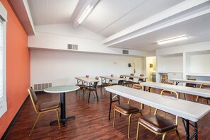 Ein Konferenzraum mit mehreren Tischen und Stühlen, weißen Wänden und einem Holzboden.