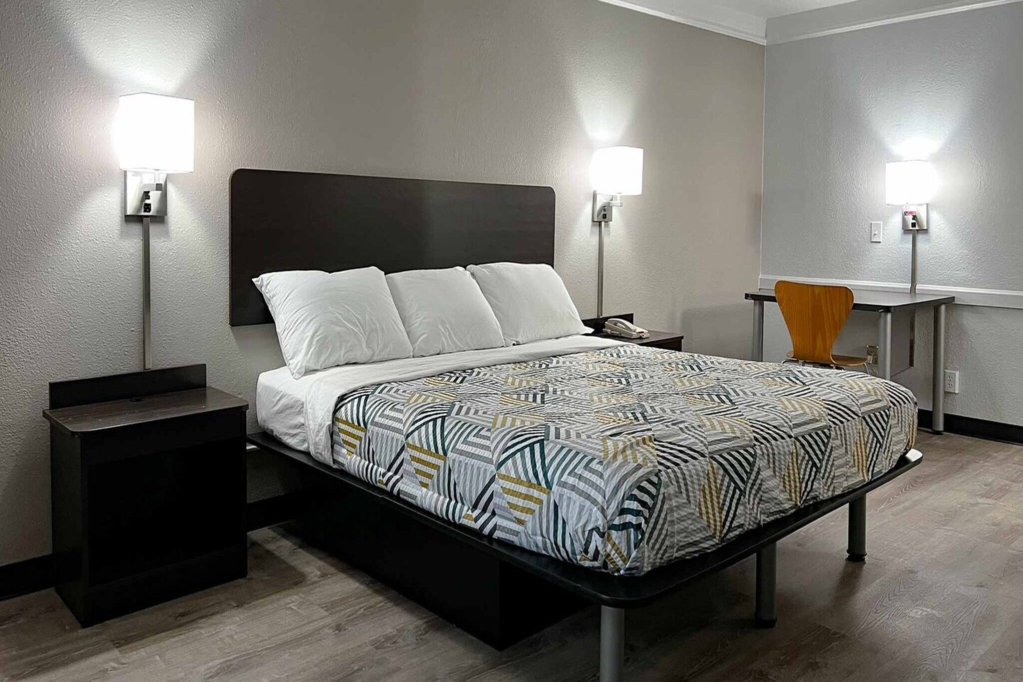 Een hotelkamer met een bed, nachtkastjes, een bureau en twee wandlampen.