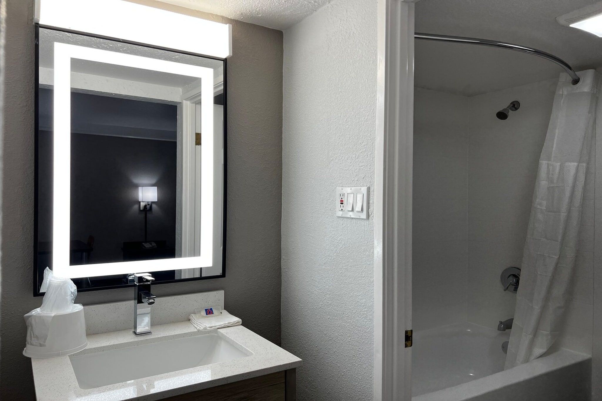 Une salle de bain avec un lavabo blanc, un miroir, une douche et un luminaire.