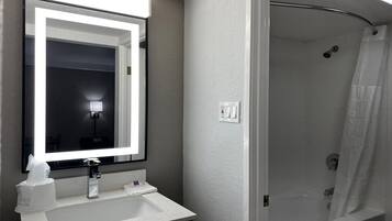 Une salle de bain avec un lavabo blanc, un miroir, une douche et un luminaire.