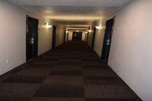 A hotel hallway with carpeted floors, doors on both sides, and wall-mounted lights. - 1 King Bed|Mobility|Tub|Nsmk|Micfridg (Hazelwood MO)