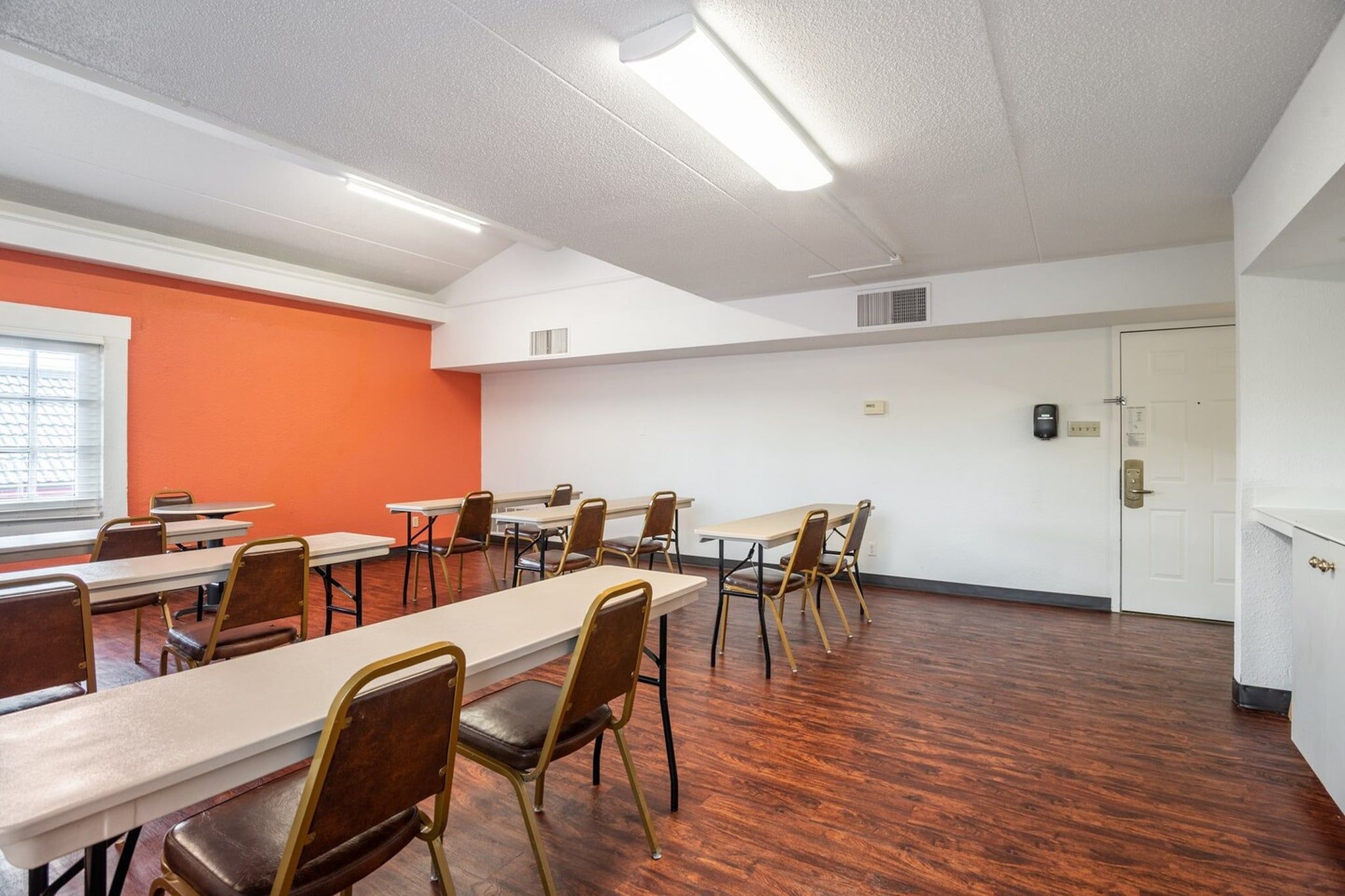 A conference room with tables and chairs, a door, and a window with blinds.