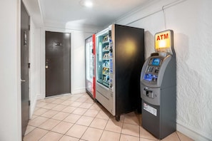 Ein Flur mit einem Getränkeautomaten, einem Kühlschrank und einer Tür.