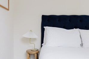 A bed with a dark headboard, white pillows, and a bedside table with a lamp. - Lovely 1BDR Split Level Flat in Islington (Greater London)