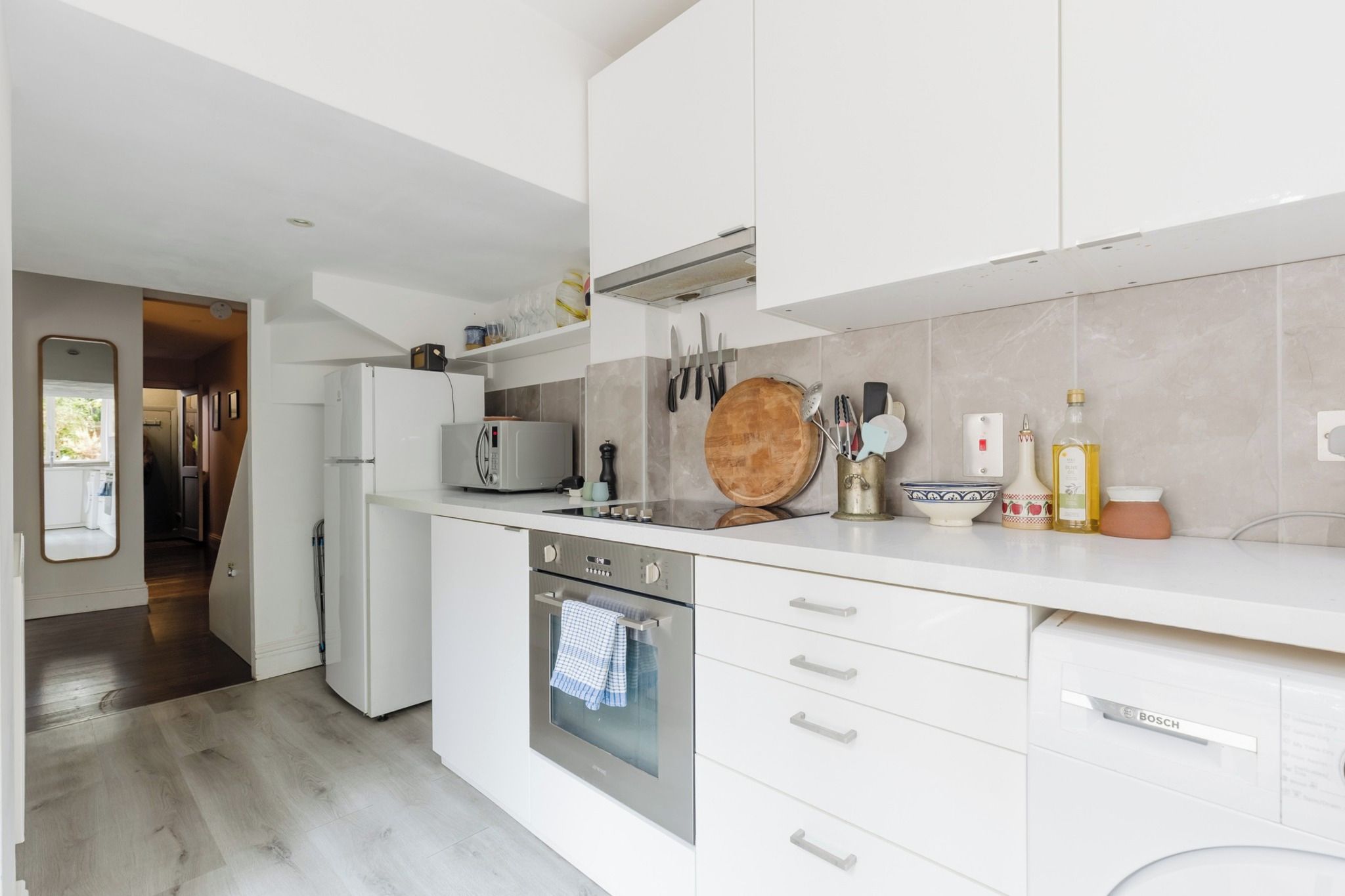 Une cuisine moderne avec des meubles blancs, un four encastré et un four à micro-ondes.