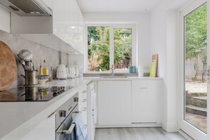 A modern kitchen with a large window, white cabinetry, and a view of the outdoors. - Lovely 1BDR Split Level Flat in Islington (Greater London)