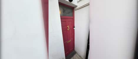 A narrow alleyway with a red door marked '82a' and a white wall.