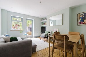 A modern living room with a sofa, a dining table with chairs, a bookshelf, and a large mirror on the wall. - Lovely 1BDR Split Level Flat in Islington (Greater London)